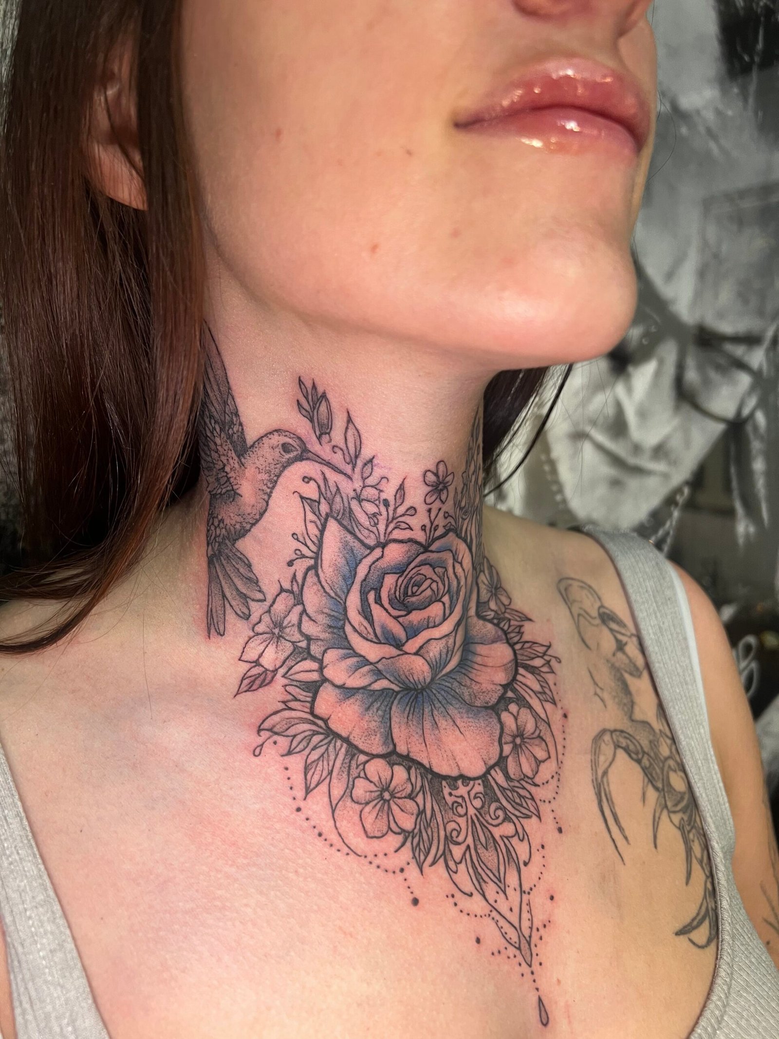 Tatouage floral noir et gris au cou représentant une rose, un colibri et des fleurs délicates en style fine line, réalisé chez KavaDerma à Drummondville.